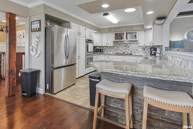 kitchen with appliances with stainless steel finishes, white cabinets, a kitchen breakfast bar, decorative backsplash, and kitchen peninsula