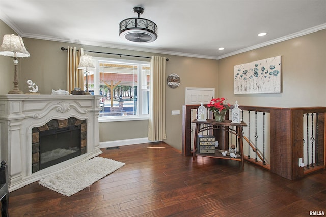 sitting room with dark wood-type flooring, ornamental molding, and a stone fireplace