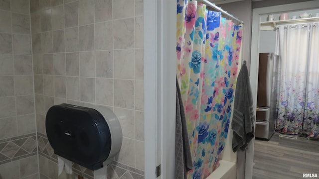 bathroom with hardwood / wood-style flooring, shower / bathtub combination with curtain, and tile walls