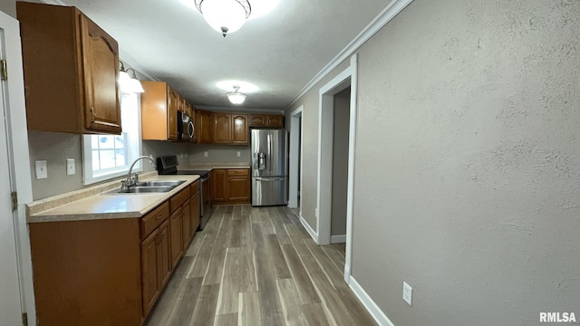 kitchen with hardwood / wood-style flooring, crown molding, appliances with stainless steel finishes, and sink