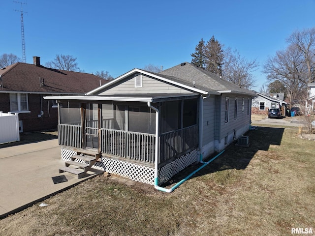 rear view of property with central AC, a sunroom, and a lawn