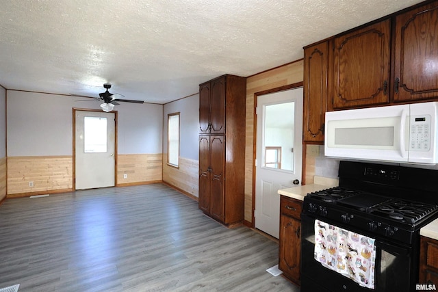 kitchen featuring wood walls, ceiling fan, light hardwood / wood-style floors, a textured ceiling, and black gas range