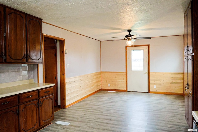 kitchen featuring ceiling fan, dark brown cabinetry, light hardwood / wood-style flooring, and wood walls