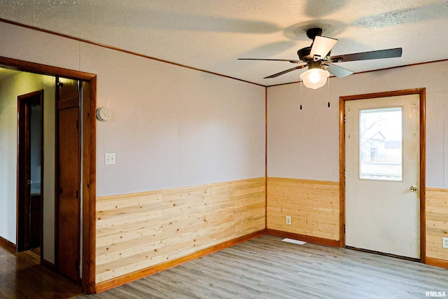 unfurnished room with hardwood / wood-style flooring, ornamental molding, wooden walls, and a textured ceiling