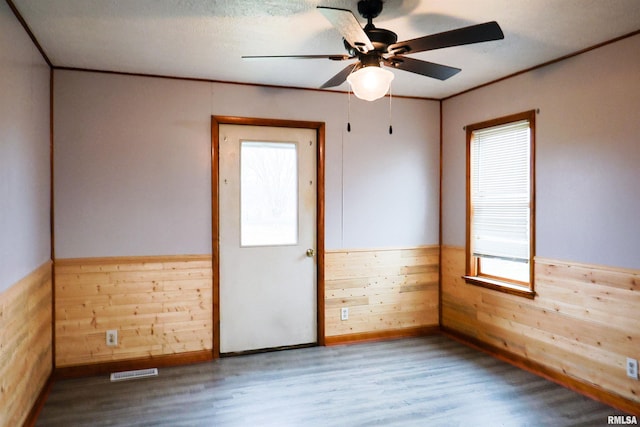 unfurnished room with wood-type flooring, ornamental molding, ceiling fan, and wood walls