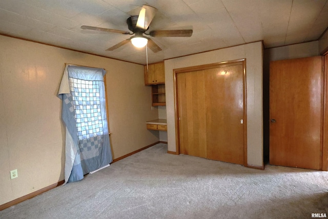 unfurnished bedroom featuring built in desk, light colored carpet, a closet, and ceiling fan