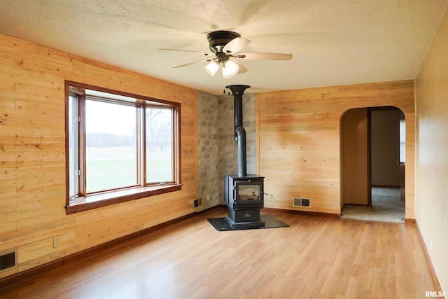 unfurnished living room with a wood stove, a textured ceiling, wooden walls, and light hardwood / wood-style floors