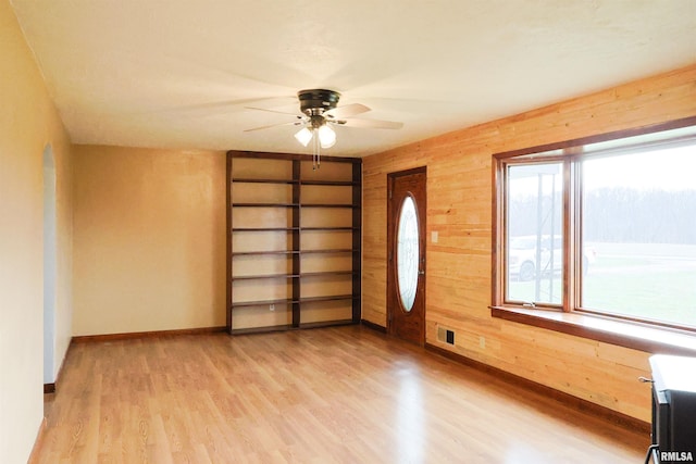 interior space featuring ceiling fan, light wood-type flooring, built in features, and wood walls