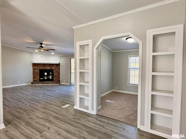 unfurnished living room featuring built in shelves, ornamental molding, a fireplace, and a textured ceiling