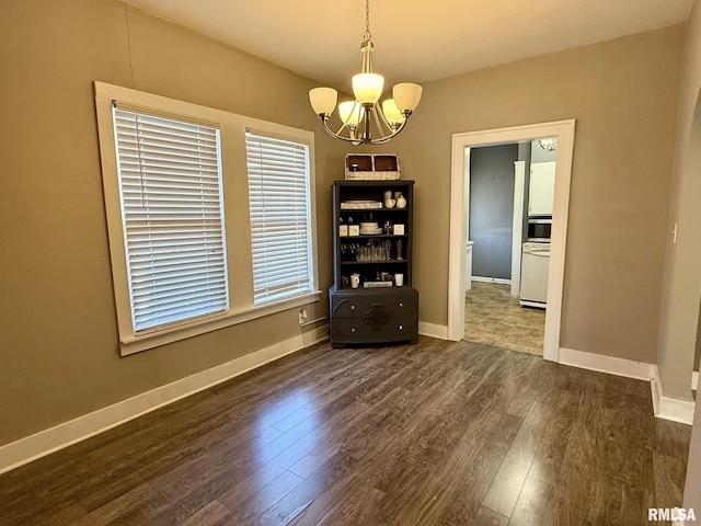 unfurnished dining area with dark wood-style floors, baseboards, and an inviting chandelier