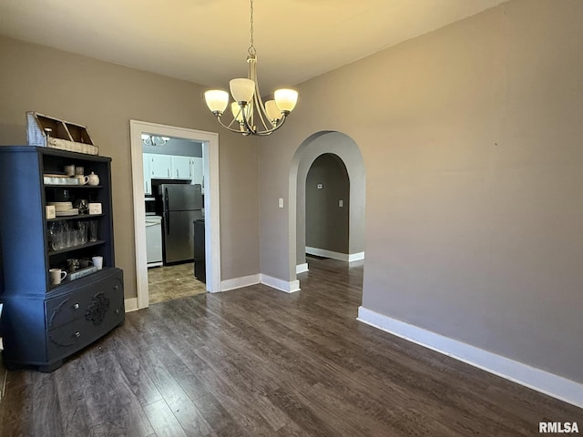 unfurnished dining area featuring arched walkways, a notable chandelier, dark wood finished floors, and baseboards