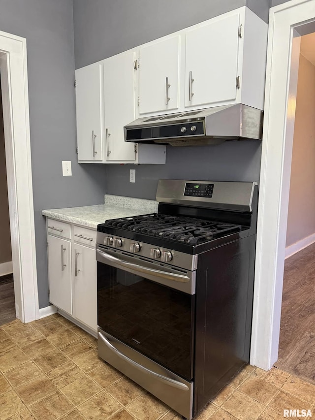 kitchen with under cabinet range hood, white cabinetry, baseboards, light countertops, and stainless steel gas stove