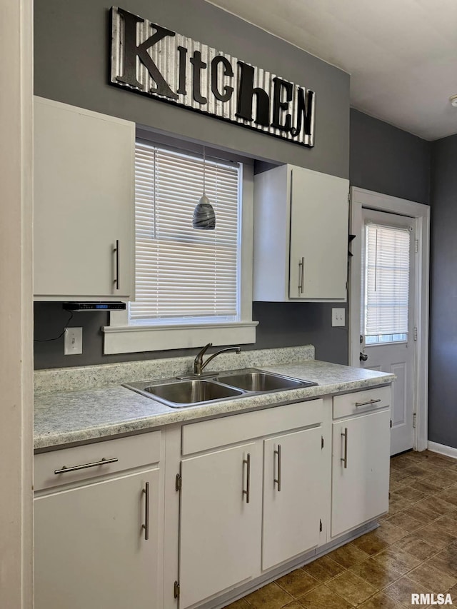 kitchen featuring baseboards, white cabinetry, light countertops, and a sink