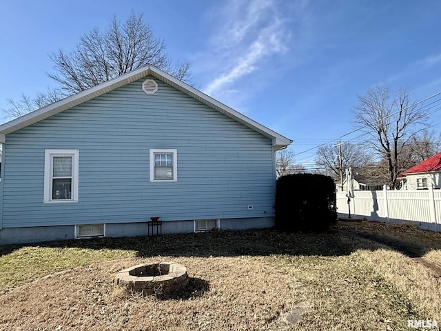 view of property exterior featuring an outdoor fire pit, a yard, and fence