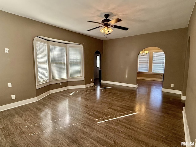 empty room with arched walkways, dark wood-style flooring, and baseboards