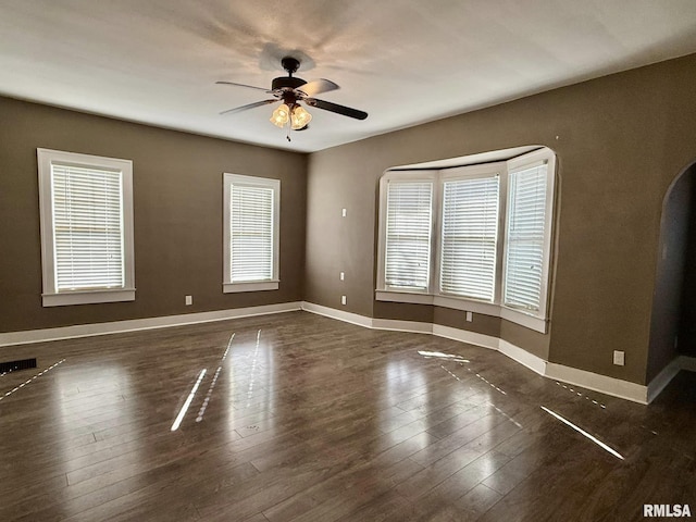 unfurnished room featuring visible vents, dark wood finished floors, a ceiling fan, and baseboards