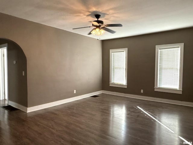 spare room with arched walkways, ceiling fan, dark wood-type flooring, visible vents, and baseboards