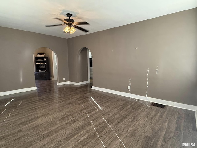 spare room featuring a ceiling fan, arched walkways, dark wood finished floors, and baseboards