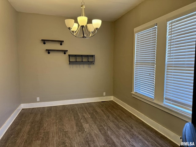 empty room featuring dark wood-style flooring, baseboards, and an inviting chandelier