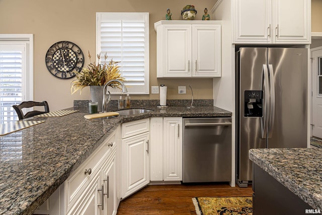 kitchen featuring appliances with stainless steel finishes, white cabinetry, sink, dark hardwood / wood-style flooring, and dark stone counters