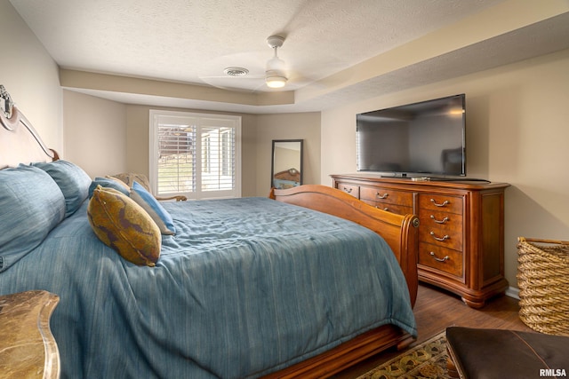 bedroom with a raised ceiling, ceiling fan, dark hardwood / wood-style floors, and a textured ceiling