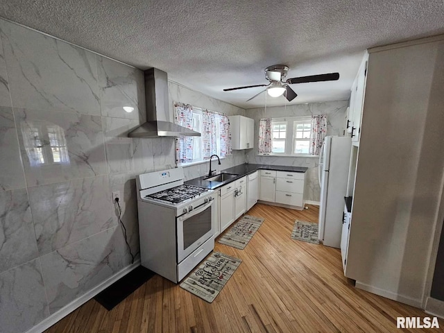 kitchen with white cabinetry, sink, light hardwood / wood-style floors, white appliances, and wall chimney exhaust hood