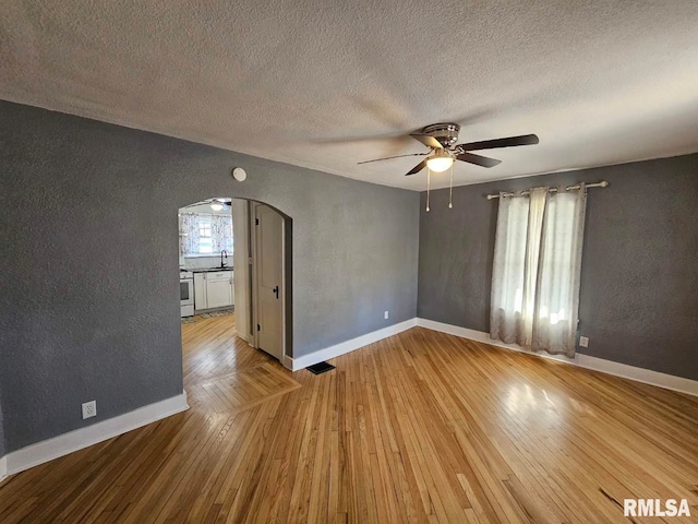 empty room with sink, a textured ceiling, ceiling fan, and light hardwood / wood-style flooring