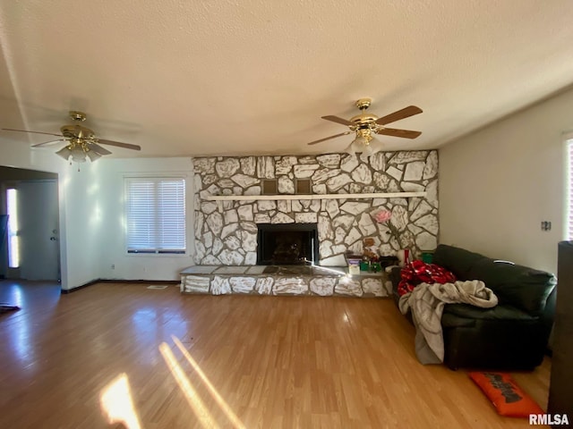 unfurnished living room with ceiling fan, a stone fireplace, wood-type flooring, and a textured ceiling