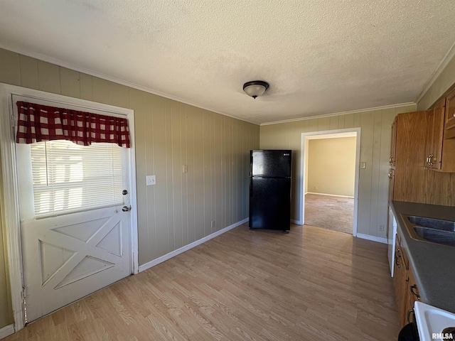 kitchen featuring sink, light wood-type flooring, ornamental molding, black fridge, and a textured ceiling