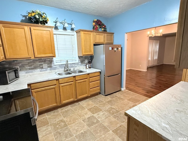 kitchen featuring appliances with stainless steel finishes, decorative light fixtures, sink, backsplash, and a textured ceiling