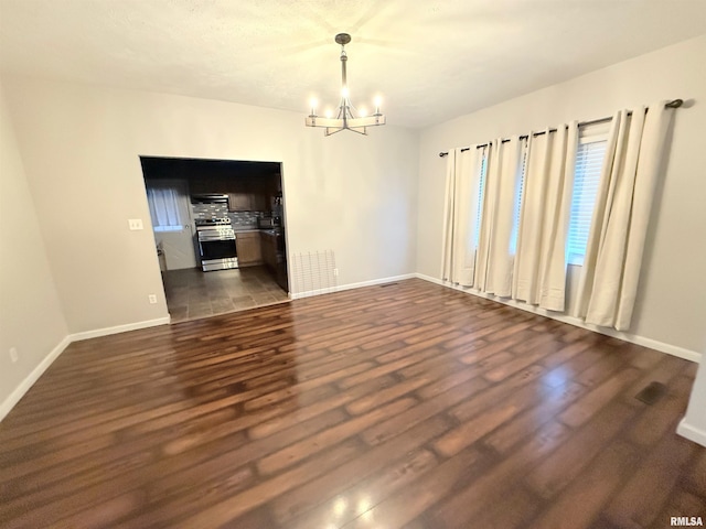 empty room with dark wood-type flooring and an inviting chandelier