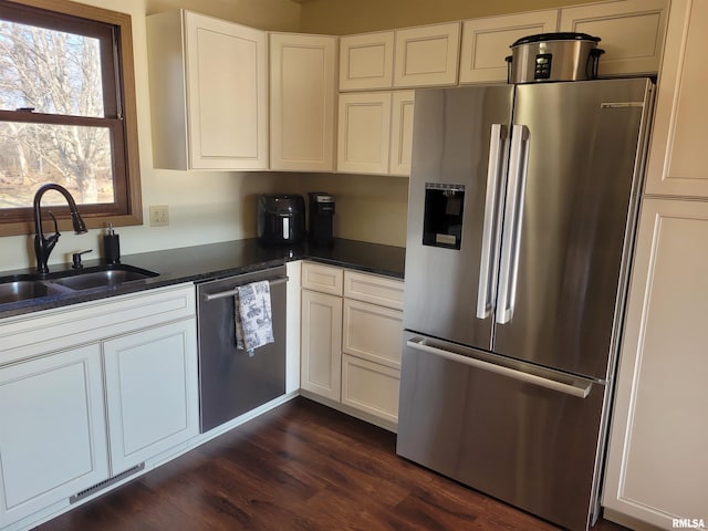 kitchen with appliances with stainless steel finishes, sink, white cabinets, dark stone counters, and dark wood-type flooring