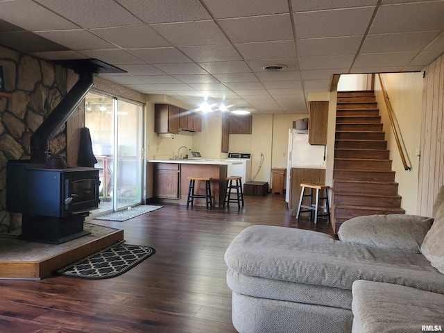 living room with dark wood-type flooring, washer / dryer, a drop ceiling, and a wood stove