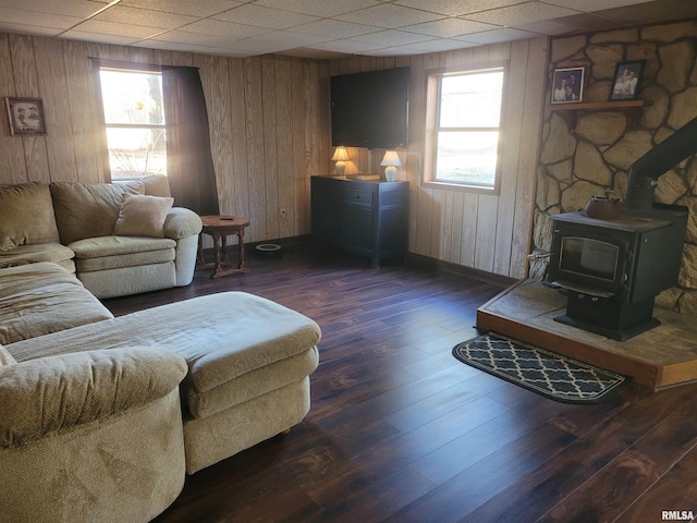 living room with dark wood-type flooring, a paneled ceiling, wooden walls, and a wood stove