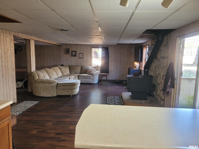 living room with dark wood-type flooring, a paneled ceiling, and a wood stove