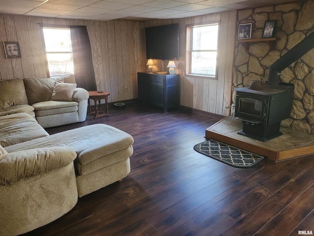 living room with a drop ceiling, dark hardwood / wood-style floors, wood walls, and a wood stove