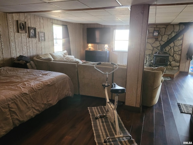 bedroom with a paneled ceiling, dark hardwood / wood-style floors, wooden walls, and a wood stove