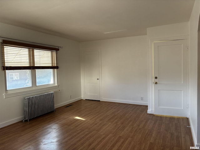 empty room with radiator heating unit and dark hardwood / wood-style flooring