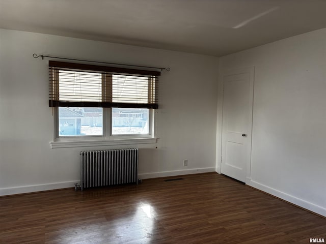 empty room with dark wood-type flooring and radiator heating unit