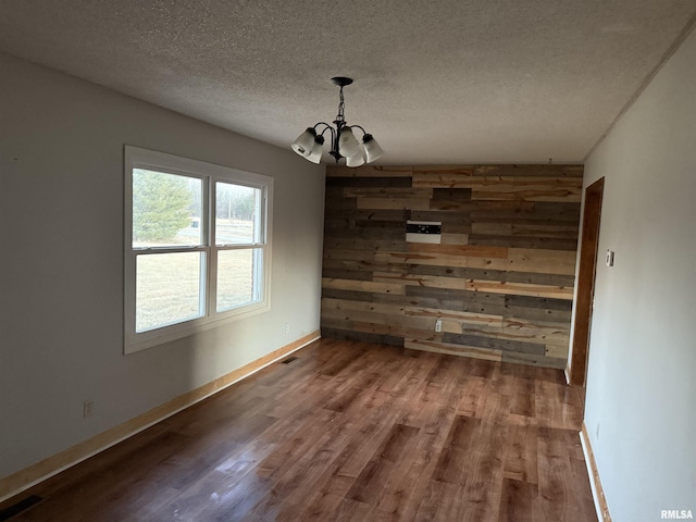 unfurnished dining area featuring hardwood / wood-style floors, a notable chandelier, wooden walls, and a textured ceiling