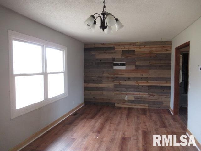 unfurnished room with dark wood-type flooring, wooden walls, a chandelier, and a textured ceiling