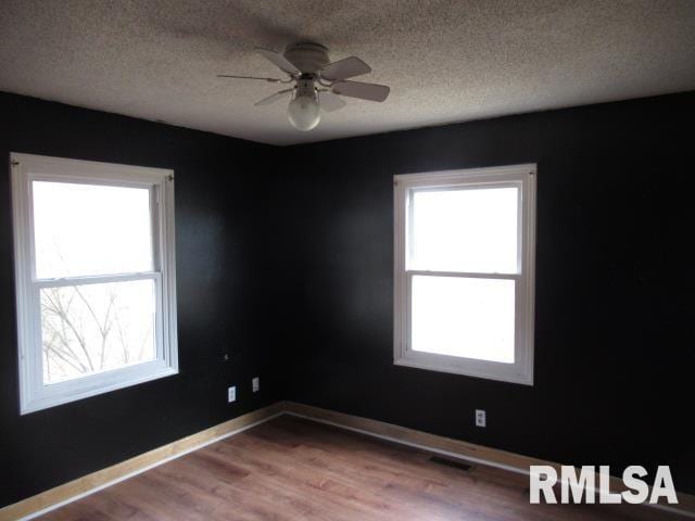 empty room with ceiling fan, wood-type flooring, and a textured ceiling