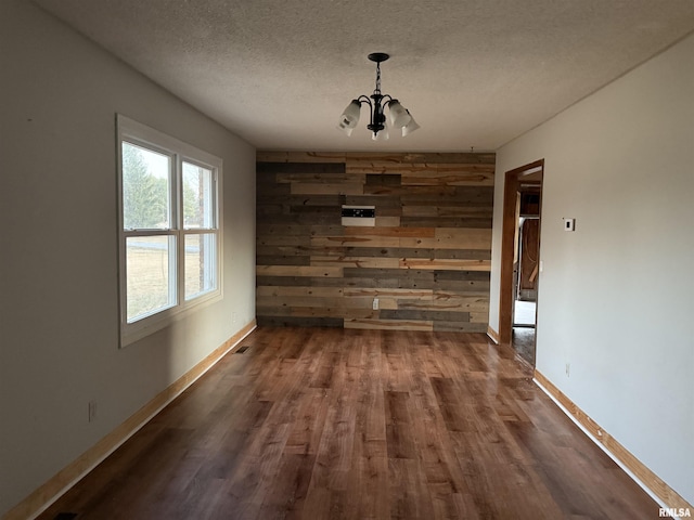 unfurnished dining area featuring wood-type flooring, a chandelier, a textured ceiling, and wood walls