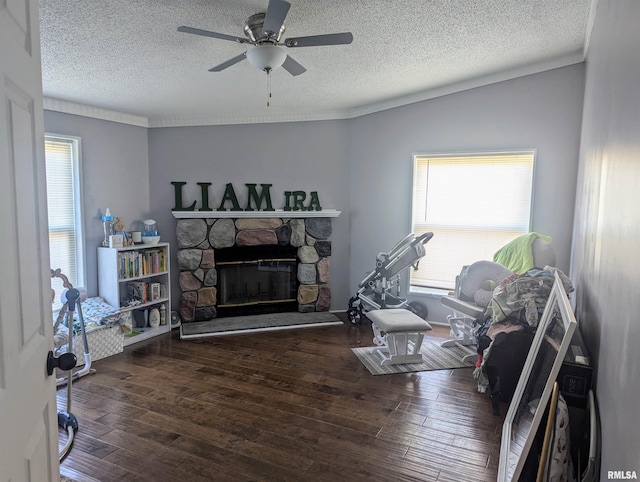 living room with dark wood-type flooring, ceiling fan, a stone fireplace, and a textured ceiling