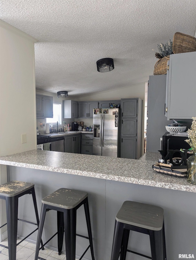 kitchen with gray cabinetry, a breakfast bar area, stainless steel fridge, and kitchen peninsula