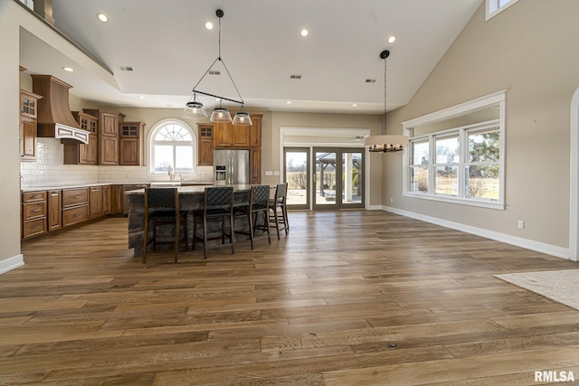 kitchen with stainless steel refrigerator with ice dispenser, a center island, hanging light fixtures, a kitchen breakfast bar, and custom range hood