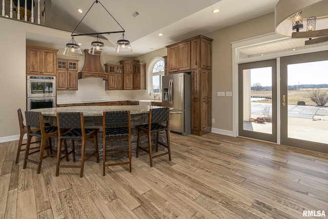 kitchen with premium range hood, appliances with stainless steel finishes, a center island, light stone countertops, and a kitchen bar