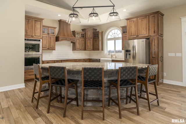 kitchen featuring premium range hood, appliances with stainless steel finishes, pendant lighting, a large island, and light stone countertops