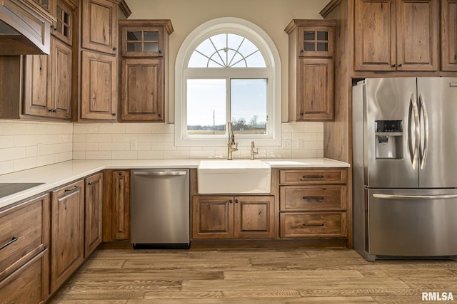 kitchen with sink, stainless steel appliances, decorative backsplash, custom exhaust hood, and light wood-type flooring