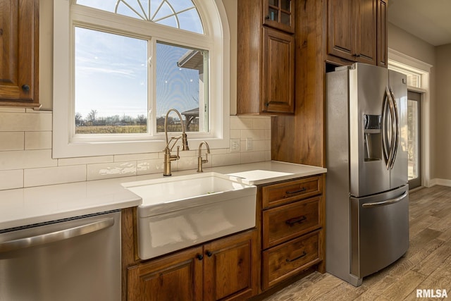 kitchen with stainless steel appliances, tasteful backsplash, sink, and light hardwood / wood-style floors